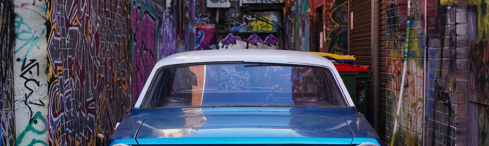 An old blue car in a garage decorated with graffiti