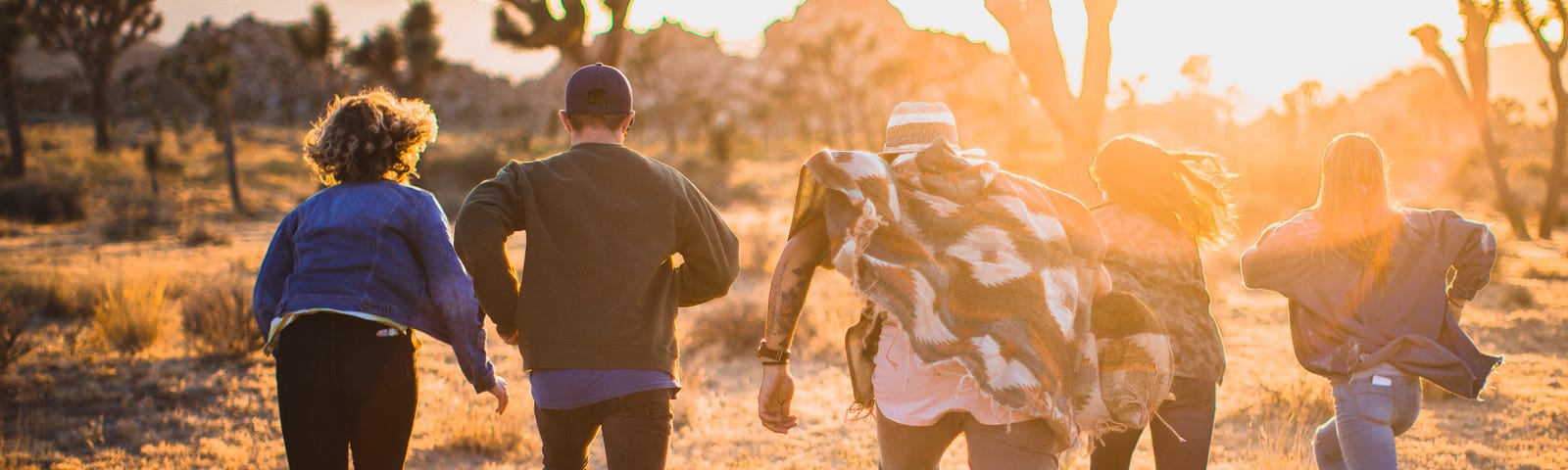 a group of 5 young people running in the opposite direction, in a desert with cactci