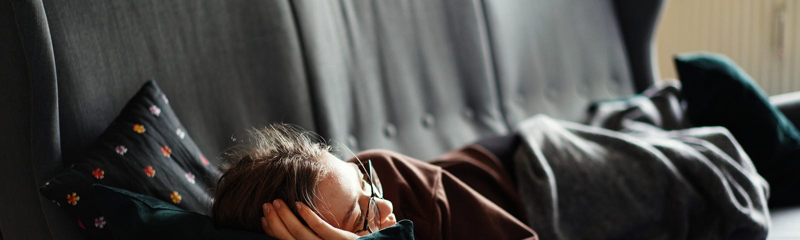 A woman laying on a gray couch wrapped in a gray blanket.