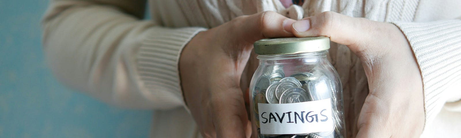 Elderly lady hands holding glass jar of coins that is labels savings.