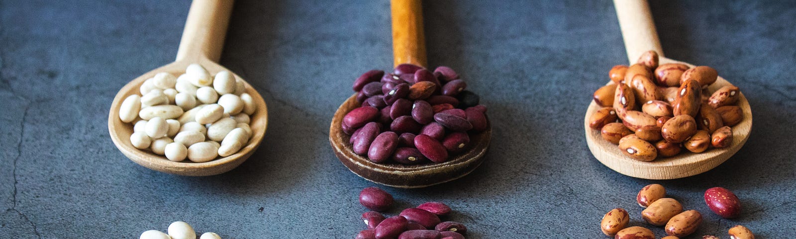 Three wooden spoons extend from the top of the image to hold soybeans. The beans are colored white, purple, and brown (left to right). Soy foods are chock full of beneficial nutrients associated with a lower heart disease risk.