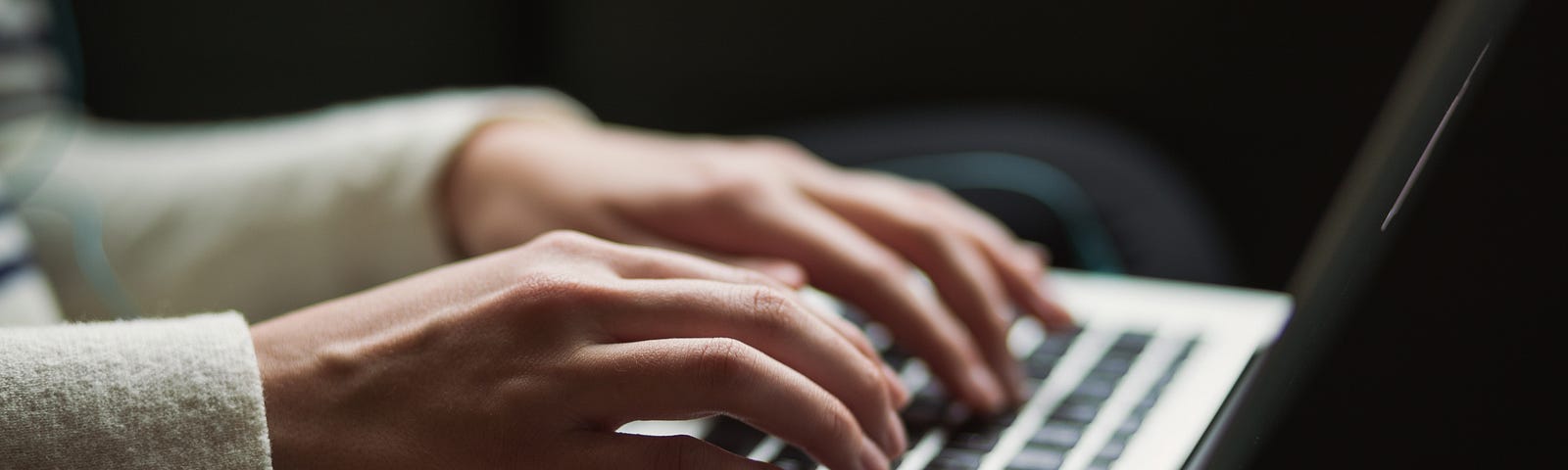 A close-up image shows a person poised with two hands hovering over a laptop keyboard, in the middle of typing.