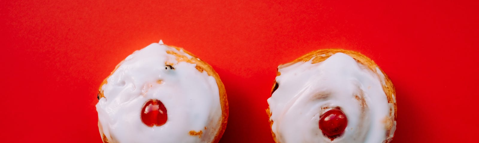 Frosted pastries with a single cherry in the middle of each, resembling breasts.