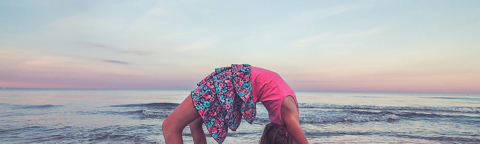 A girl doing a back bend on a beach.