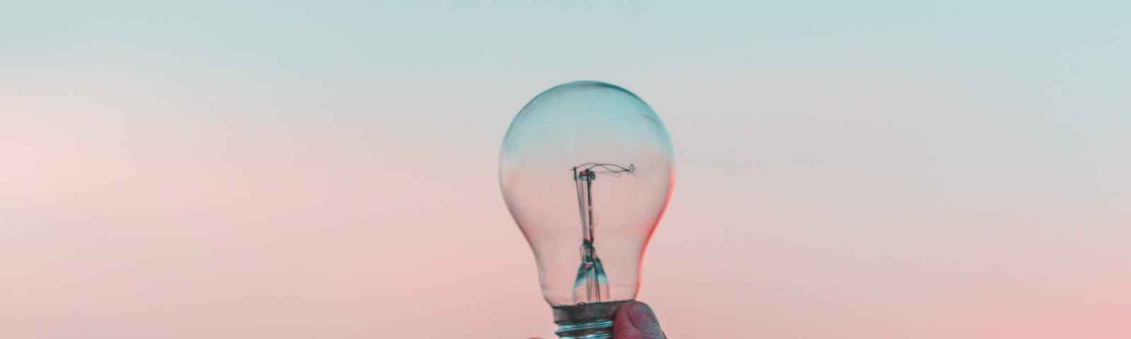 A person holding up a lightbulb on a gradient background.