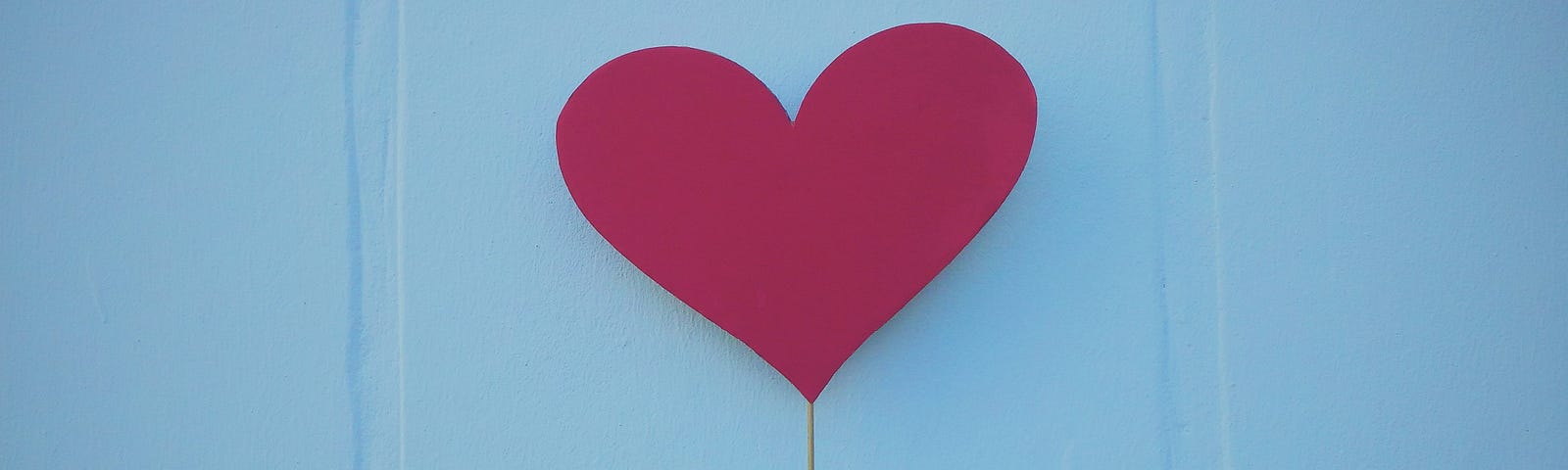 Image of a person holding up a red heart made of construction paper.