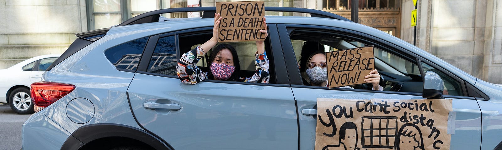 People hold signs from a car window