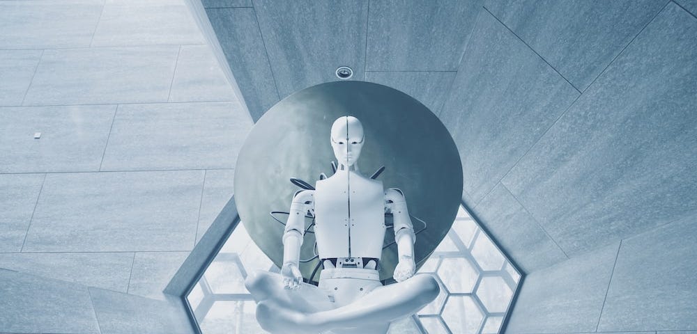 A white robot floats in mid-air in lotus yoga pose while wires are attached to it, keeping it grounded in a hexagonal-shaped gray room