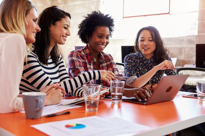 Mulheres diversas reunidas, discutindo em volta de um computador