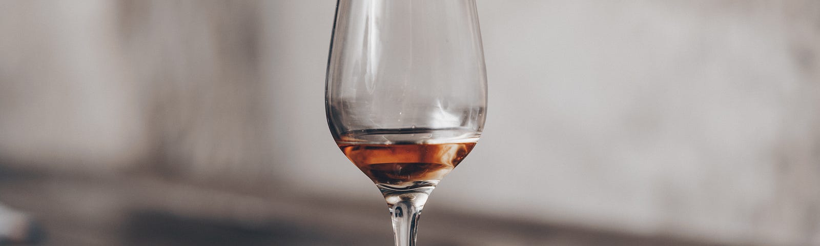 Image of a clear wine glass with a bit of red wine in it on a brown wooden table.