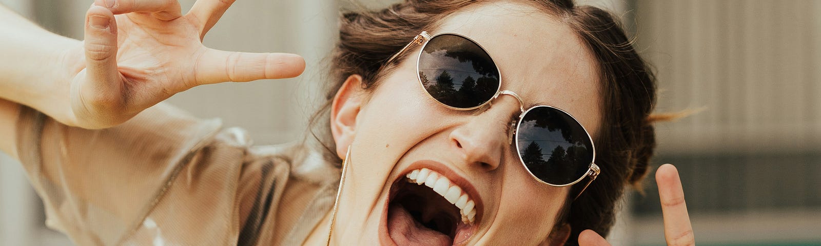 Smiling woman wearing sunglasses, making peace signs, exuding playfulness and joy. A perfect reminder to relax and have fun.