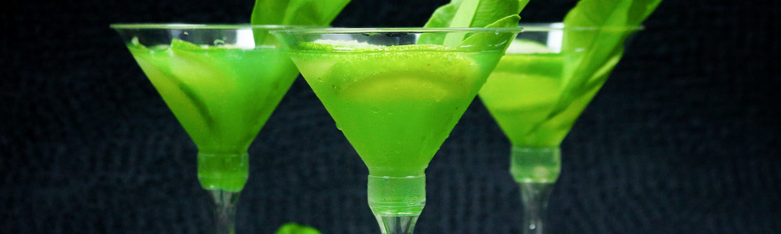 3 lime drinks in champagne style glasses lined up against a dark background.