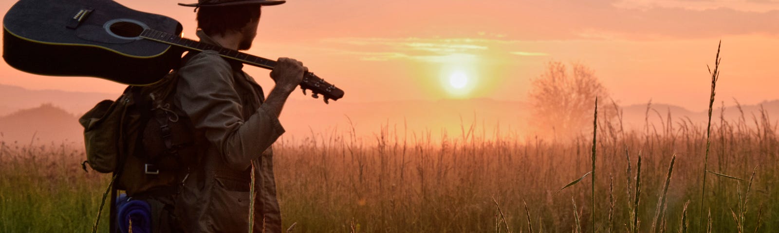 a man wandering through a meadow at sunrise, a pack on his back, a guitar resting on his shoulder