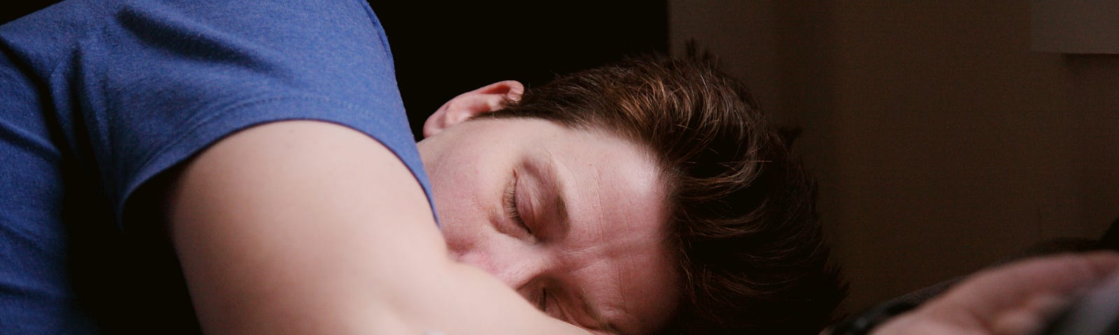 Man wearing a blue shirt sleeping on his side with his head resting on one arm.