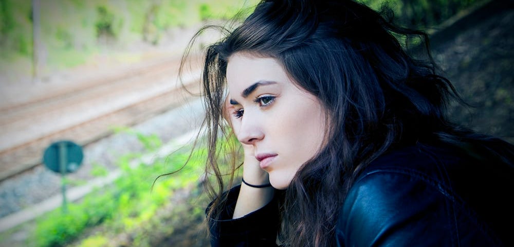 Woman sitting outdoor during daytime holding her head in her hand