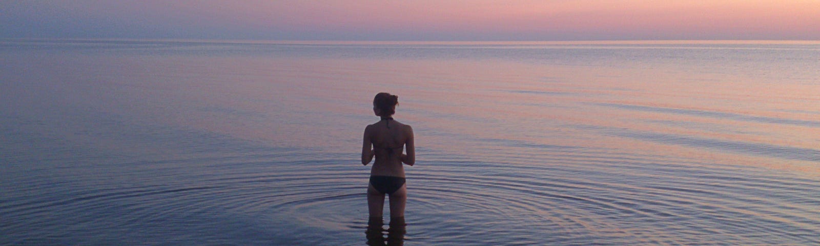 Woman paddling in water at sunset