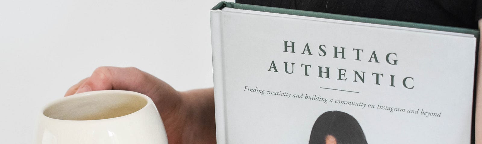 Woman with holding a cup and a book with writing on the book that says Hashtag authentic.