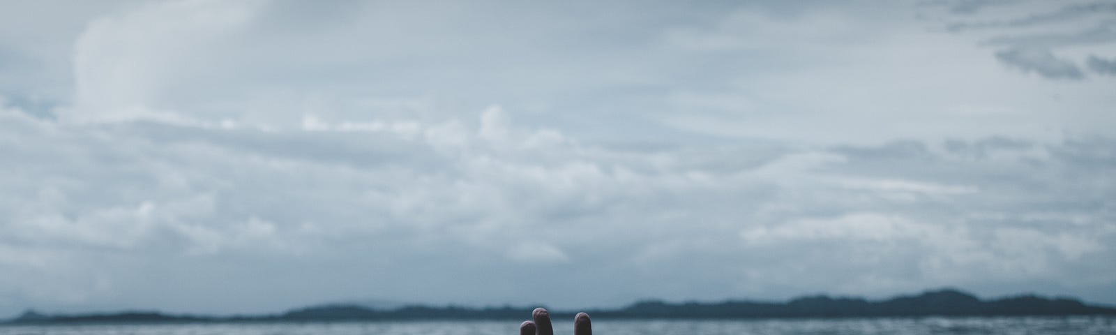 Human hand reaching out of the water in the middle of the ocean