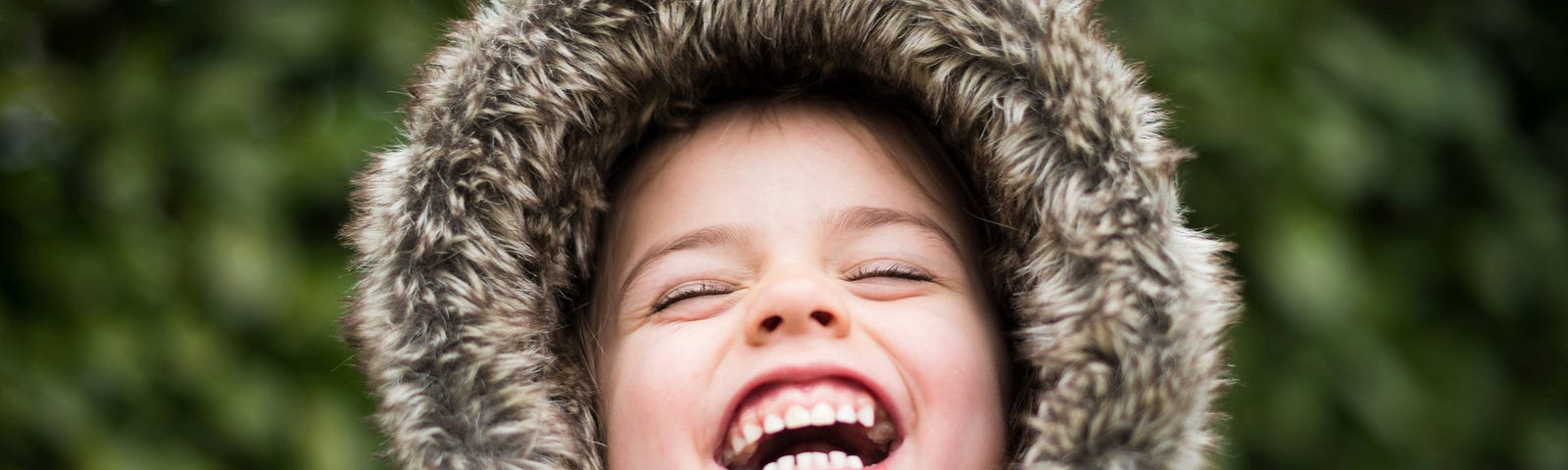 A toddler in a winter boat and hood laughs with joy