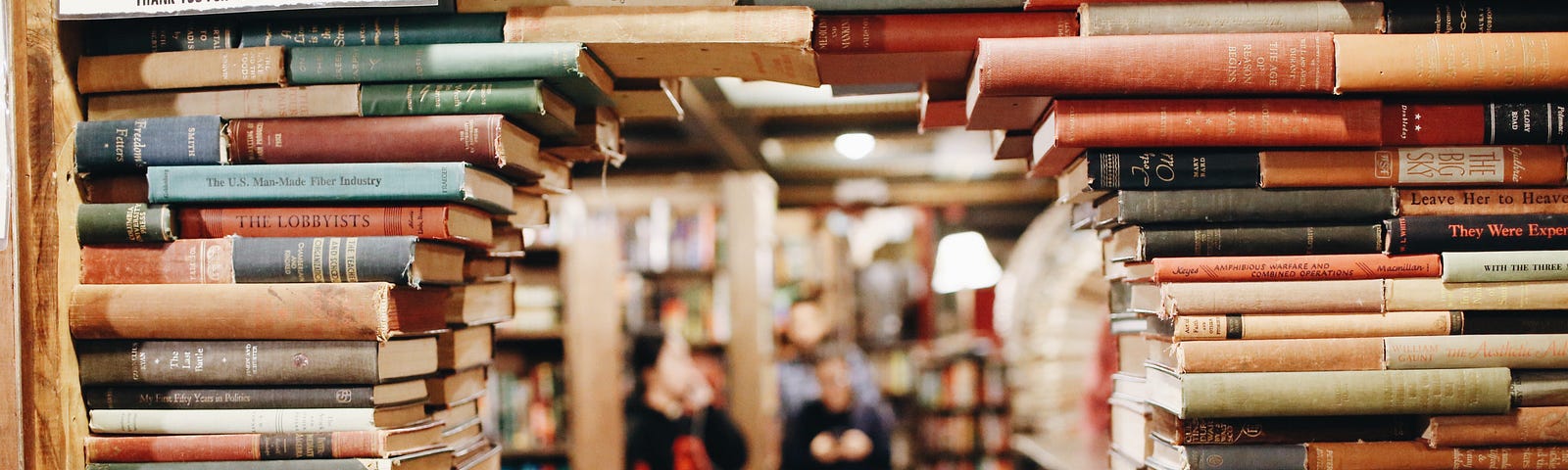 A shelf of books stacked with a hole in the middle to see through to people reading in the background