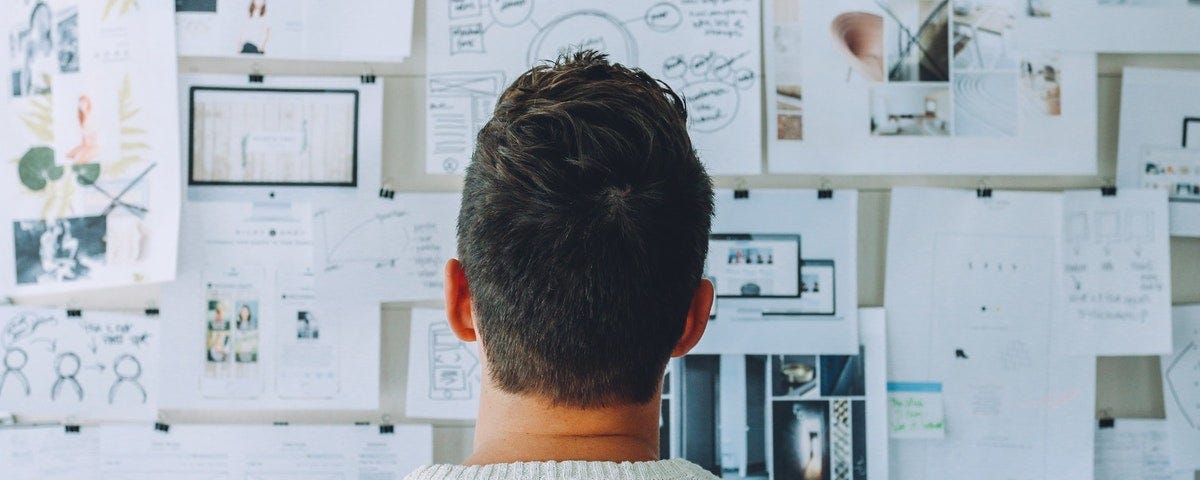 Man looking at a board filled with several sheets of paper pinned to the board