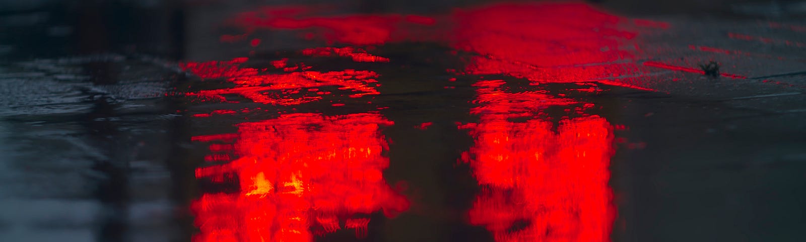 Rain puddle, bathed in red night light.