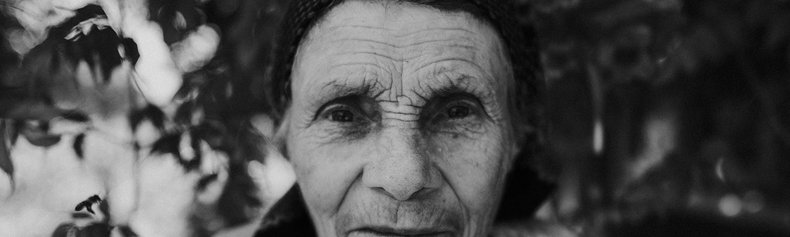 A black and white image of an old woman staring directly at the screen.