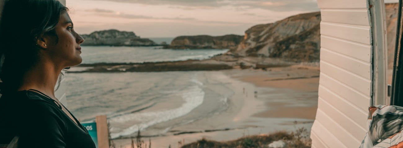 An individual sitting in a van with the ocean in the background.