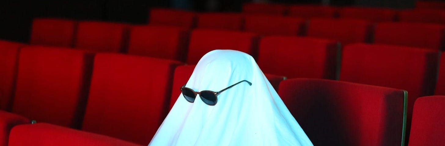 A ghost (white sheet over an object) with sunglasses in movie seats.