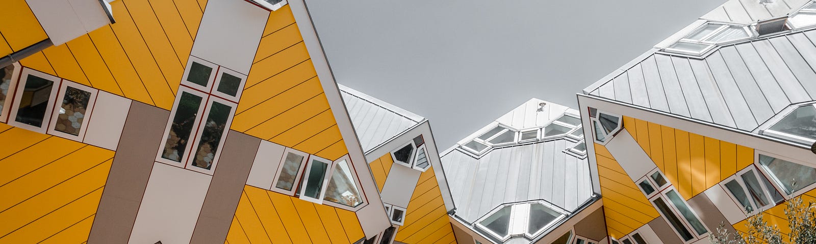 An unusual upward view of cube-shaped, bright yellow houses, against a grey sky.