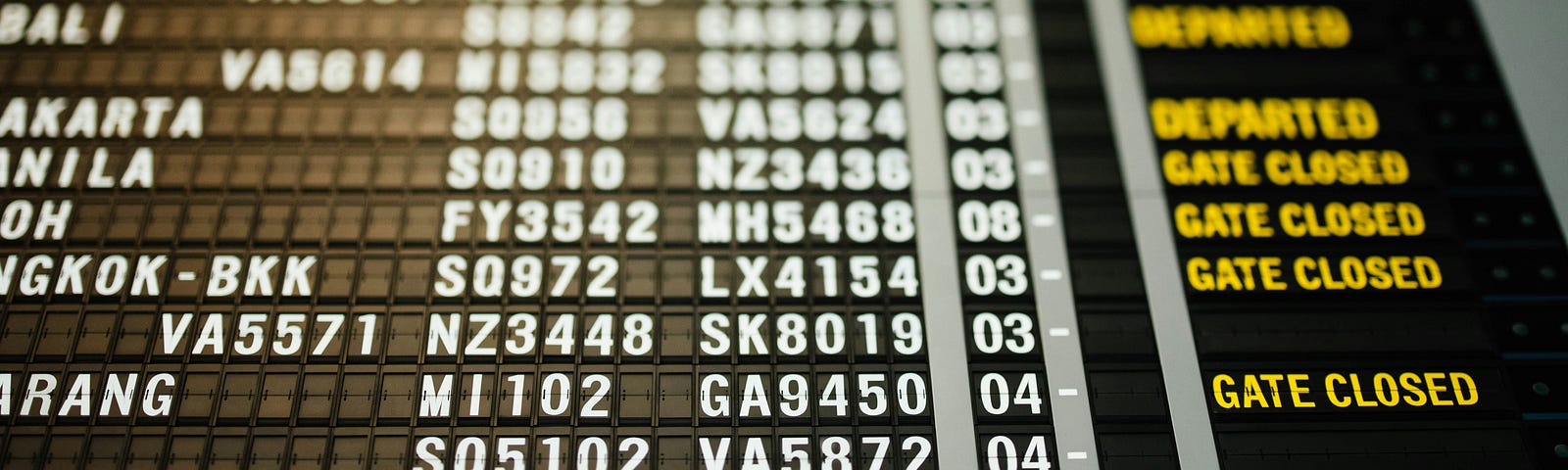 A photograph looking up at an airport departure board, showing ‘gate closed’ for many flights.