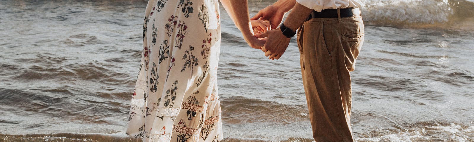 Couple holding hands on beach facing each other.