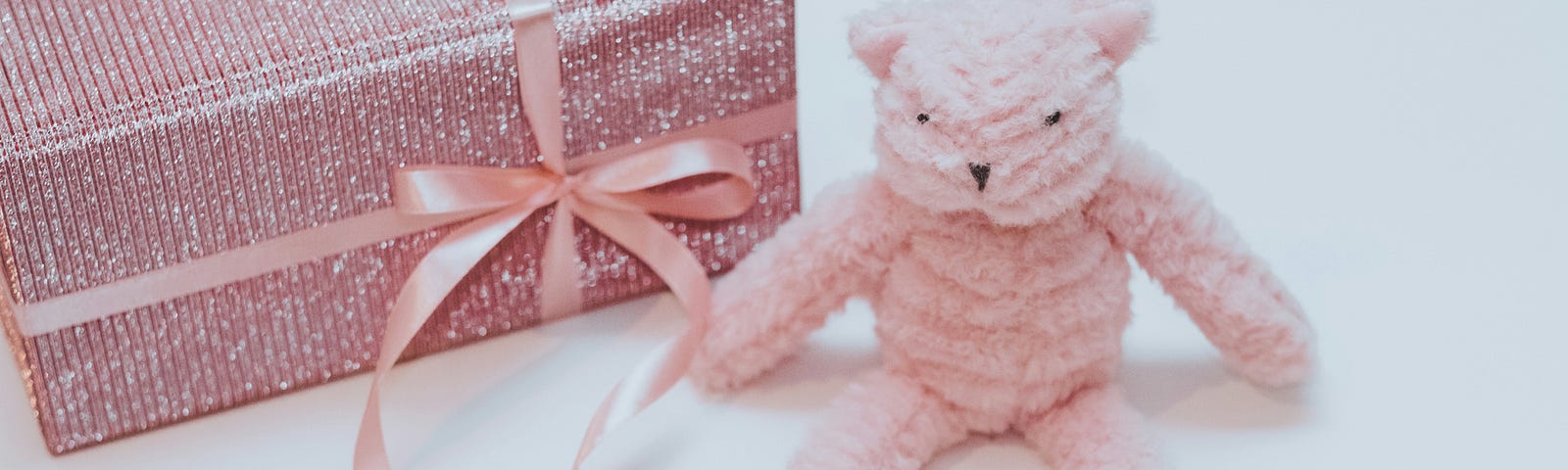A plush pink teddy bear sits next to a dazzling pink-wrapped gift.