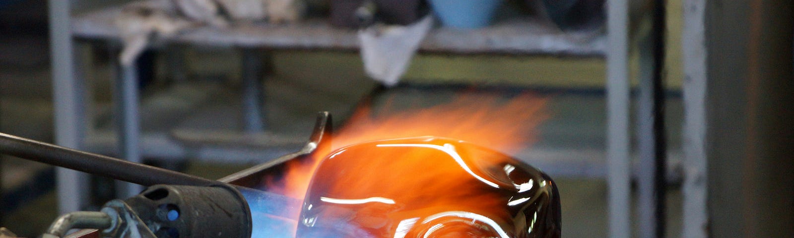 Artist using a blue flamed torch to fuse and heat glass into artwork.