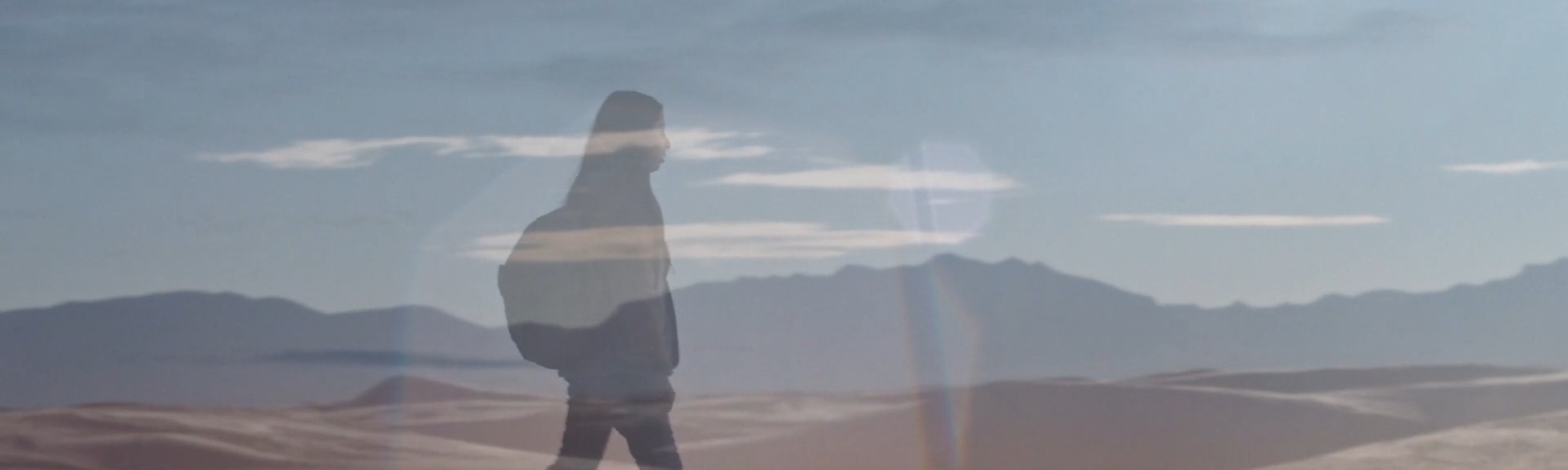 Still from AWAY TOGETHER by Sana Malik, featuring an image of protagonist Ayah carrying a backpack walking toward the right of the still, overlaid on top of an image of the New Mexico landscape.