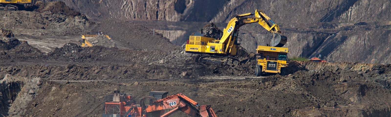 Earth movers and excavators mine for coal in an open-air strip mine.