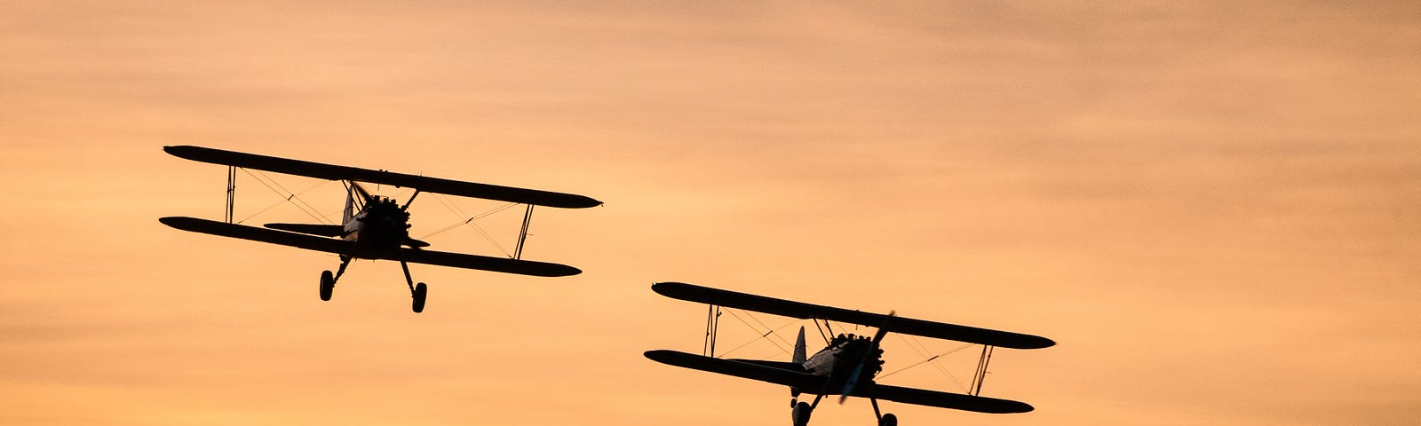 Two biplanes flying through a sunset