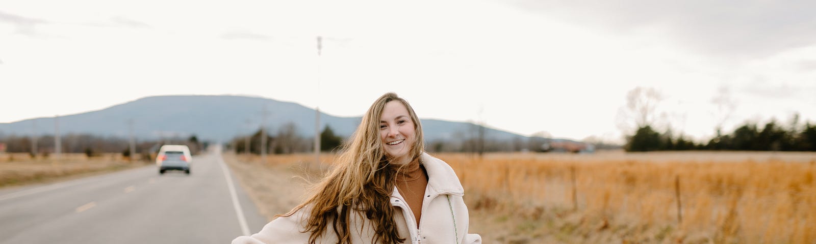 A young girl is hitchhiking next to a highway. Photo by Brooke Cagle on Unsplash