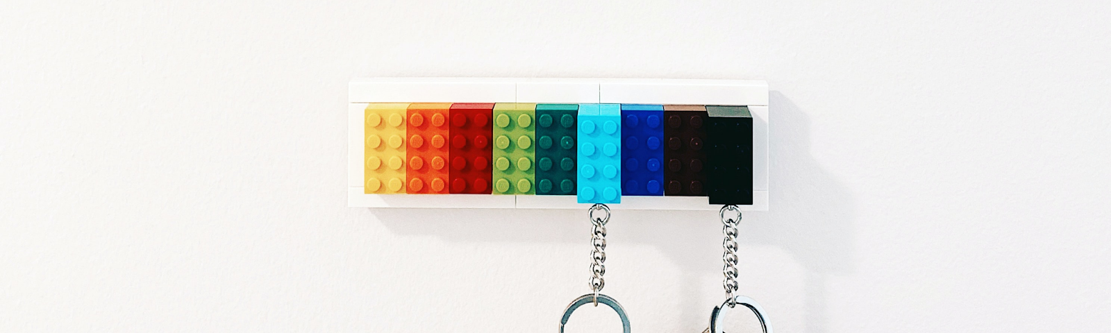 A couple of keys are suspended  from a row of colorful legos that form a key hook.