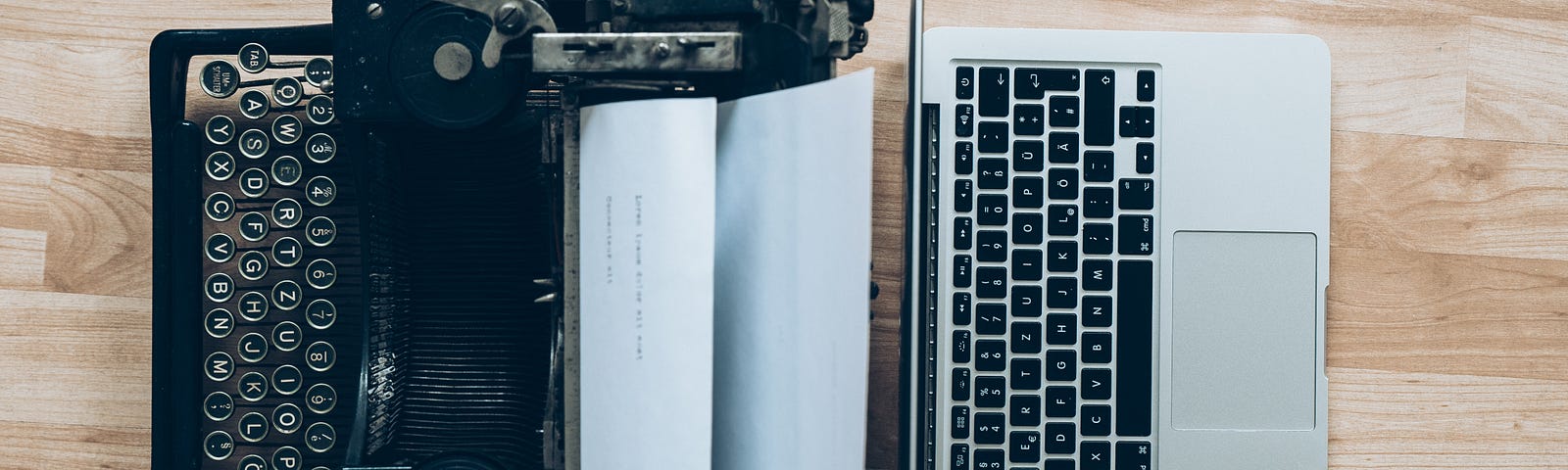 A typewriter with paper next to a modern laptop.