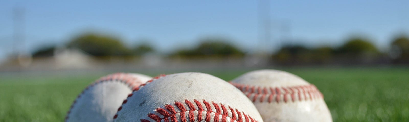 Three scratched baseballs in the grass.