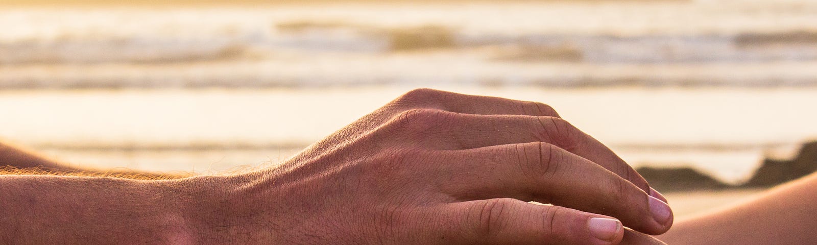 Close-up of hands being gently held with golden light at the beach.