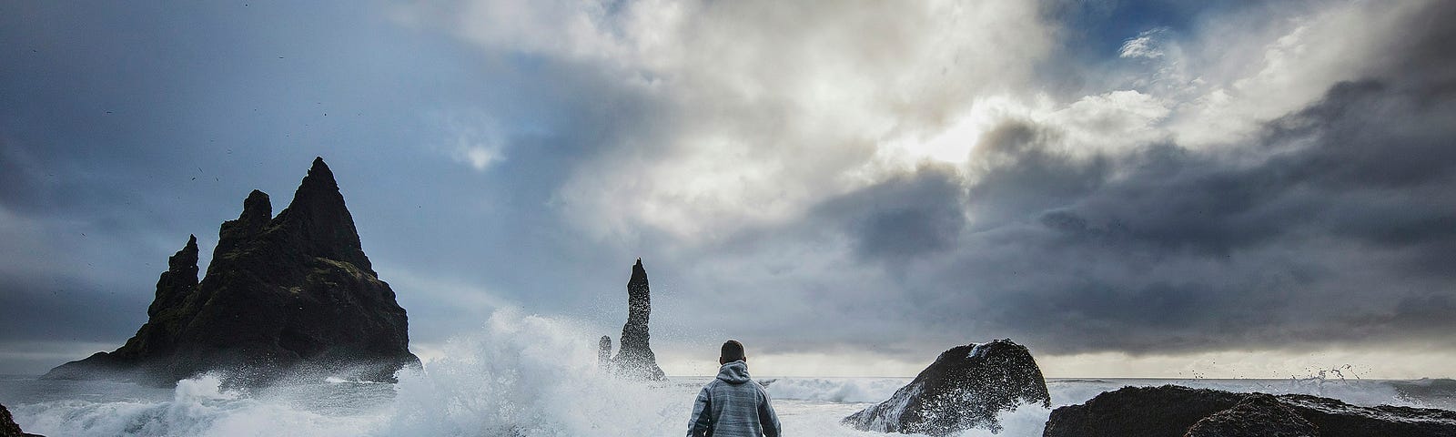 A lonely man walking where the wind and the waves throw themselves on the rough rocky beach