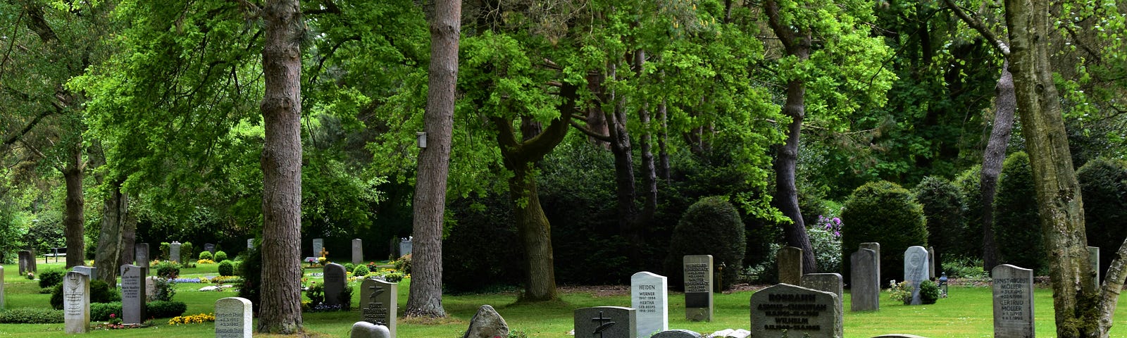 Beautifully kept cemetery, freshly mowed, cloudy day, extremely green grass and bushes around it.