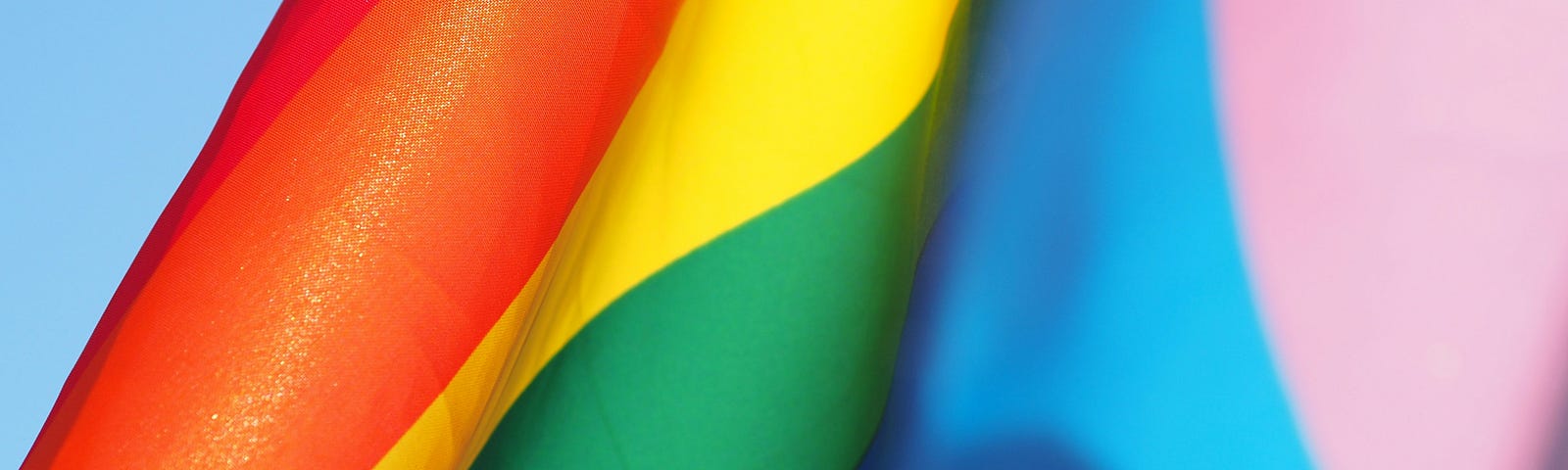 Close-up of the colorful rainbow stripes on a PRIDE flag, against a bright blue sky.