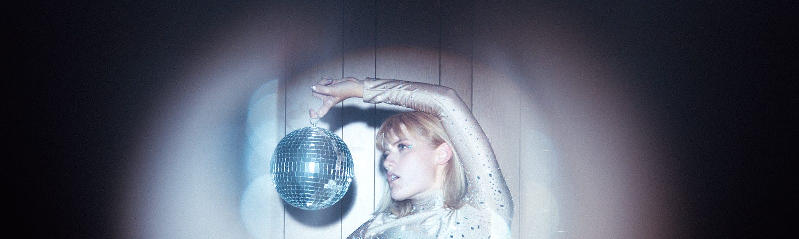 Dark background with a girl wearing a sparkly white top and holding a silver glitter ball.