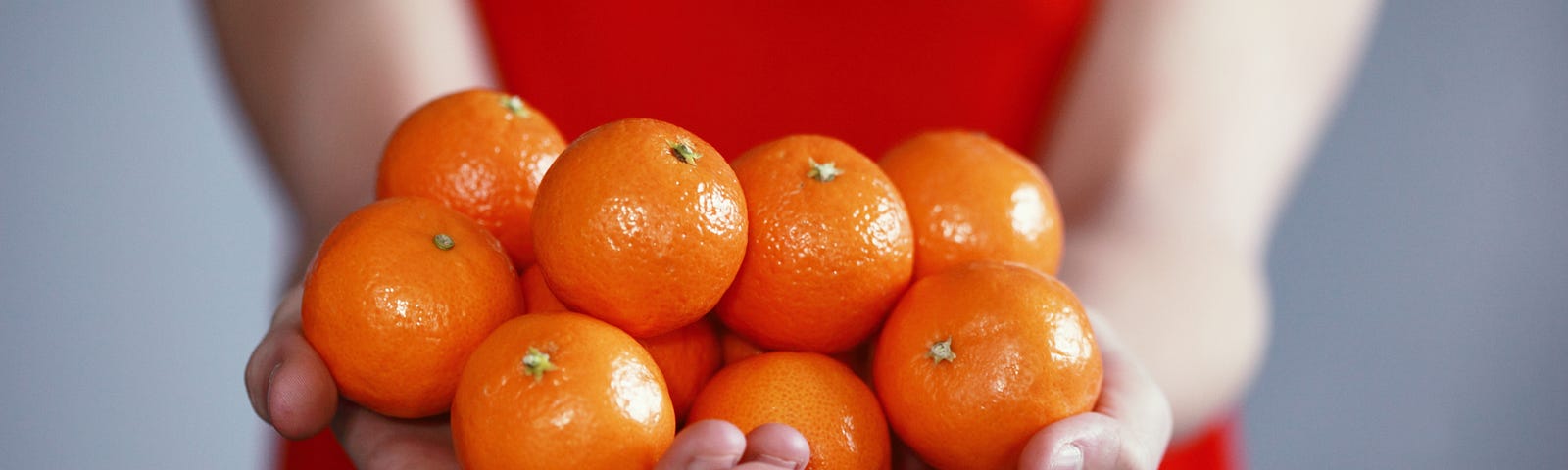 A woman wearing a red dress, holding a bunch of small oranges