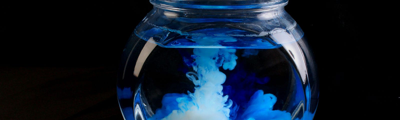 Bulbous glass filled with water in which blue color that slowly dissolves.