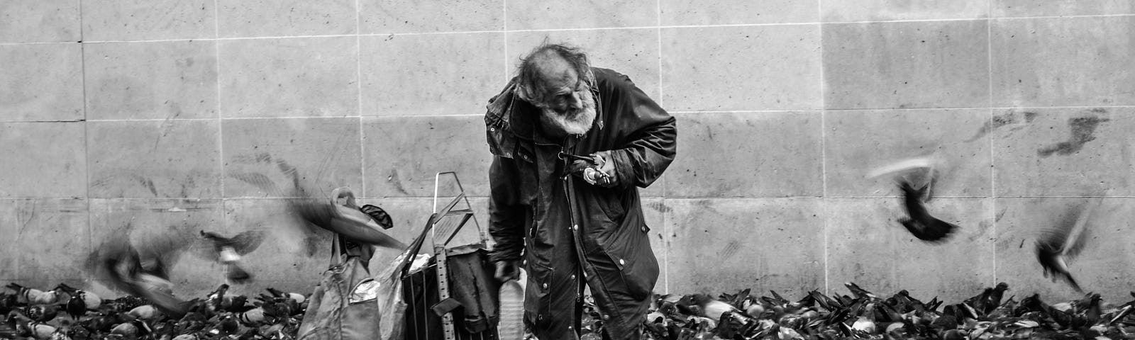 black and white image of homeless man among many pigeons