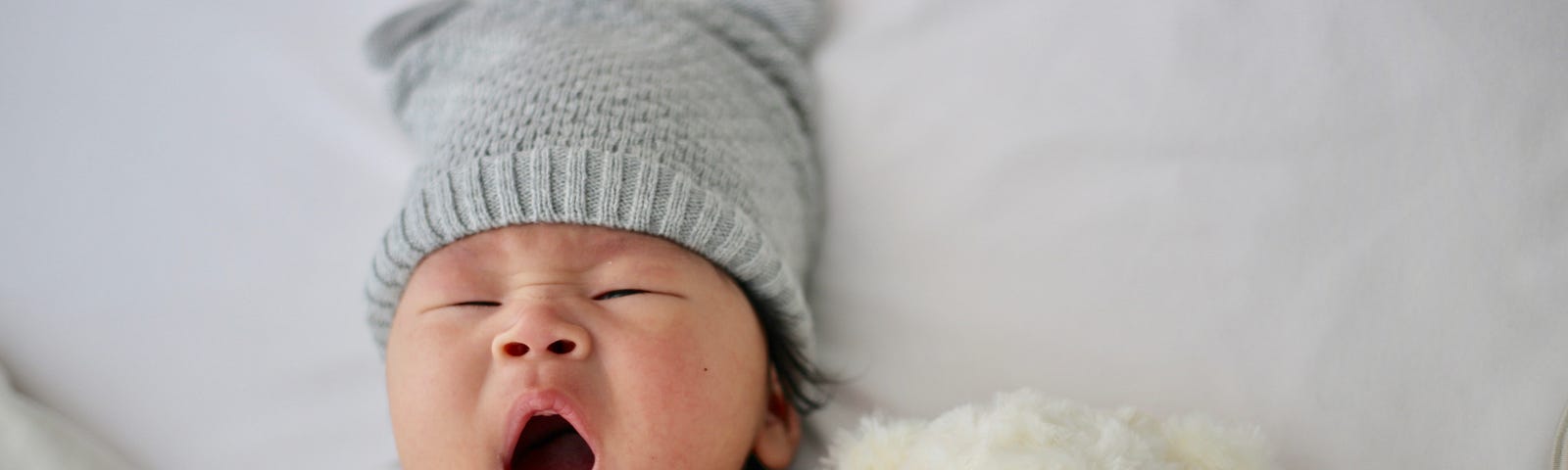 A baby, with a cap on his head, lies in bed, his white stuffed bear next to him. Sleep apnea is when an individual experiences pauses in their breathing while they sleep. Such pauses can last for several seconds to minutes and occur many times throughout the night.